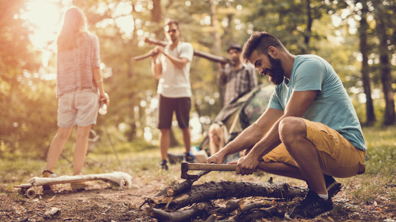 Man chopping wood with friends while camping