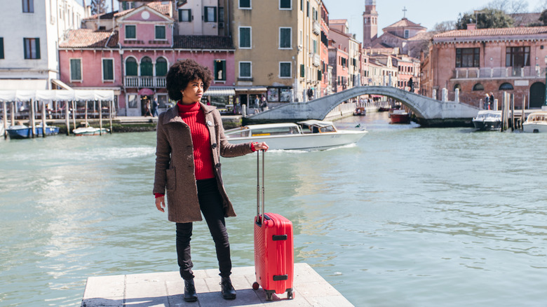 Woman posing with a red suitcase along a canal in Venice, Italy