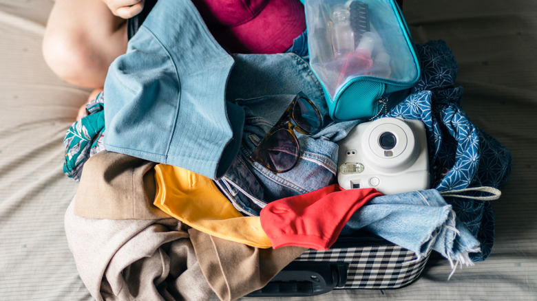 An open suitcase with clothes and a Polaroid camera