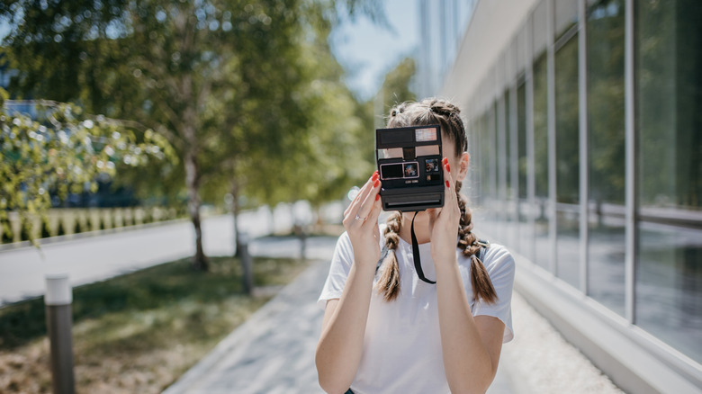 Young woman facing camera taking a photo with her own portable camera