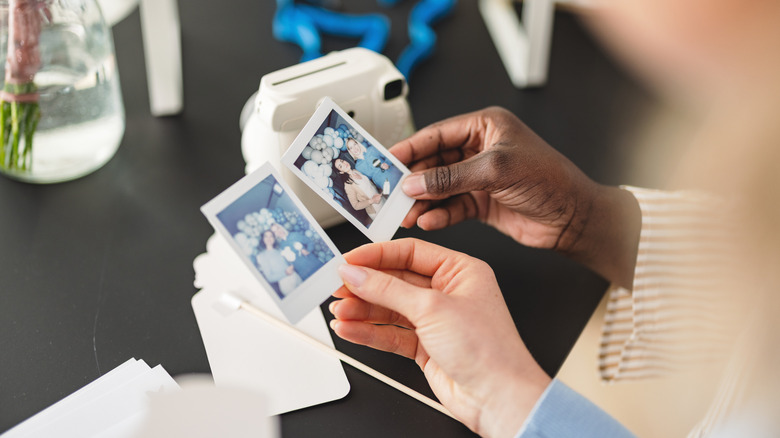 Two people holding photos from portable cameras