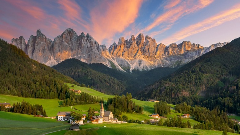 A small village in a green meadow in Italy with the Dolomite Mountains in the distance