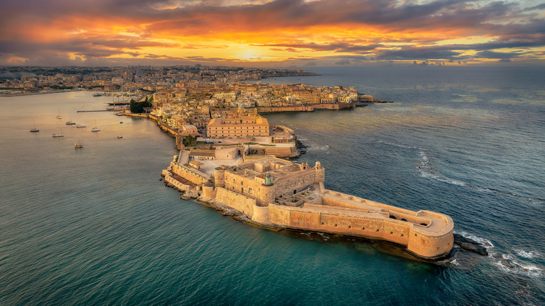 The walls and buildings in the Italian town of Ortigia surrounded by the sea at sunset