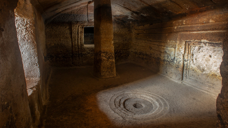 Interior chamber of a Domus de Janas featuring a stone column and concentric circles etched into the floor