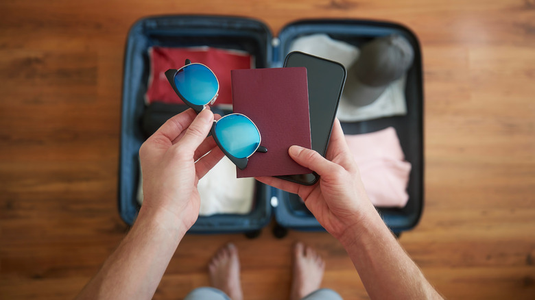 Hands holding sunglasses, a passport, and a mobile phone