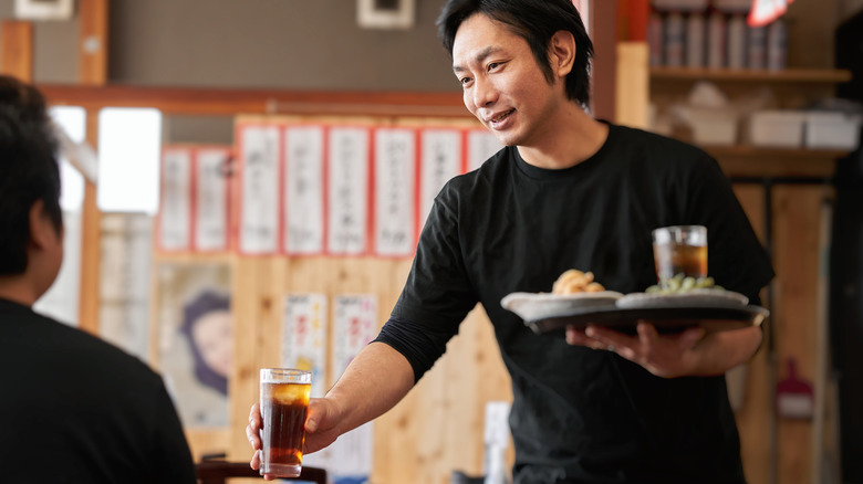 A Japanese server in a black shirt handing out a drink to a customer