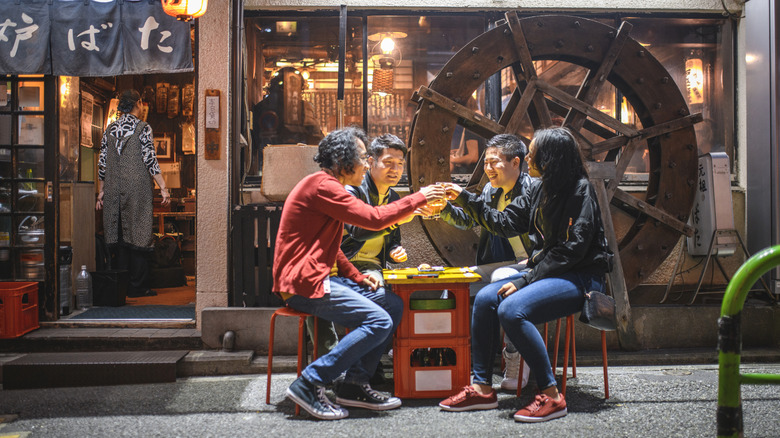 A group of friends clinking glasses while sitting outside a Japanese restaurant