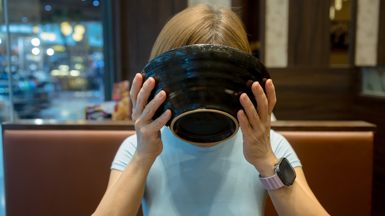 Women drinking ramen from a bowl, face hidden by bowl