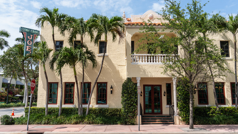Street view of the yellow facade and palm trees outside Joe's Stone Crab