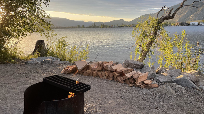 Firewood and a fire in a fire pit at a lakeside campsite at sẁiẁs Provincial Park, overlooking Osoyoos Lake