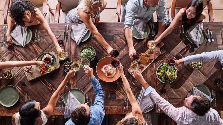 Aerial view of people around a wood table toasting with wine glasses