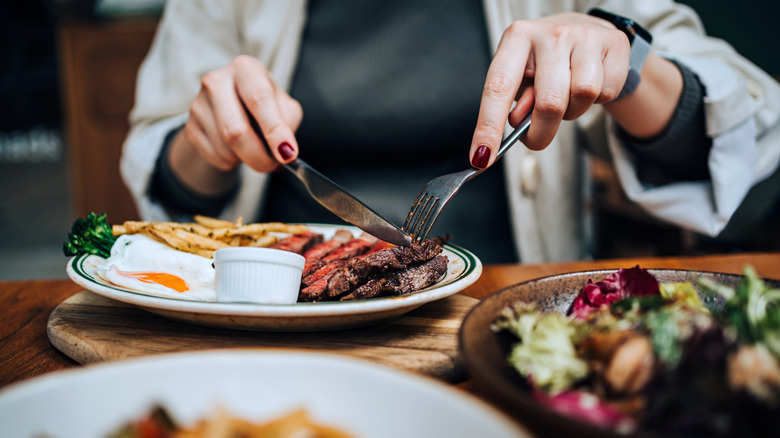 A woman eating a juicy, grilled fillet steak along with assorted dishes on dining table