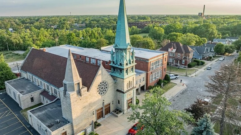 First Evangelical Lutheran Church in Blue Island, a white stone building with a blue spire, beside other brick structures with trees and bridges in the background