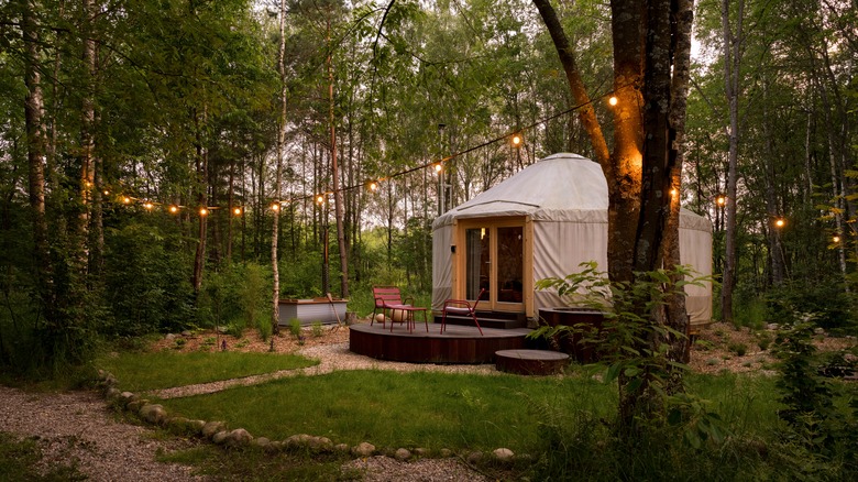 Beautiful yurt tent with charming fairy lights surrounded by a green forest.