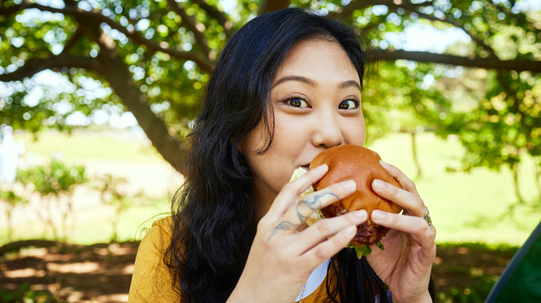 Woman eating burger outside under tree