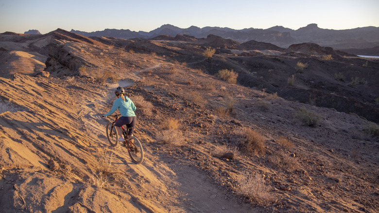 A woman climbs a dirt trail in the desert on a bike