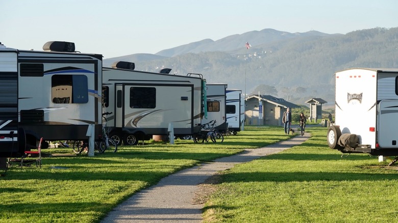 A couple walking a dog walk on a path between grassy RV sites at Francis Beach Campground.