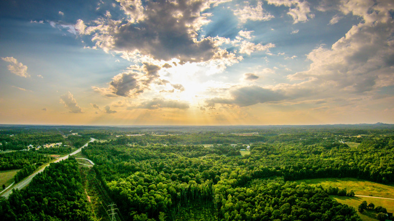 Sun shining with beams over trees, roads, and clouds in York County, South Carolina.