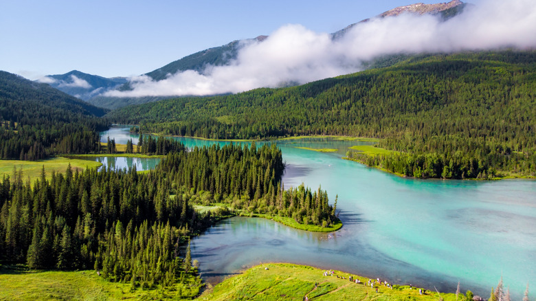 Kanas River coursing through vibrant green grass and trees with a cloud laying across the mountaintop