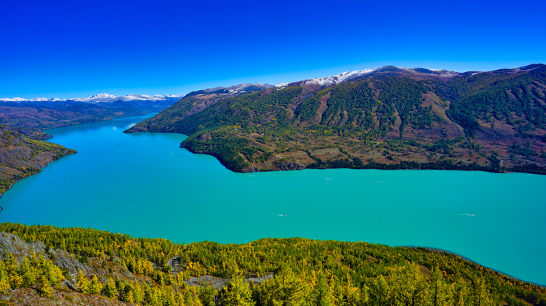 Boats on Kanas Lake, China, with sapphire blue waters and snow-tipped, sculpted green mountains surrounding the shore