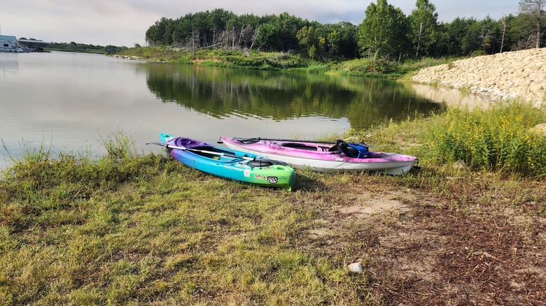Two kayaks on grass next to lake surrounded by forest