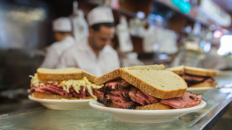 Pastrami sandwiches on a counter with chefs out of focus in the background