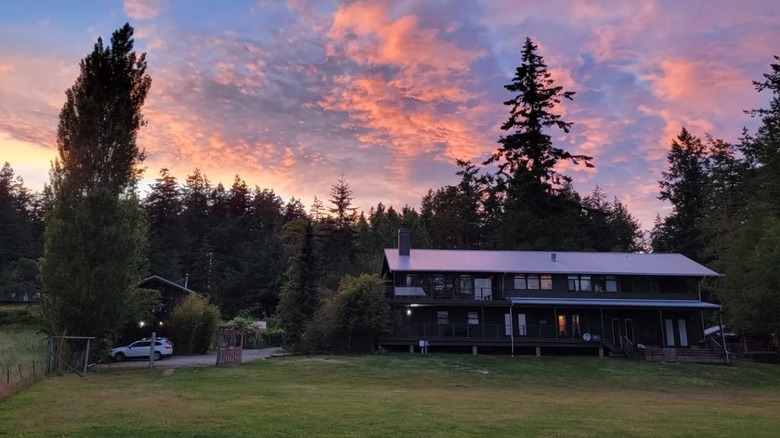 Fiery sunset clouds behind a forest and the wooden Pebble Cove Farm inn on Orcas Island, Washington