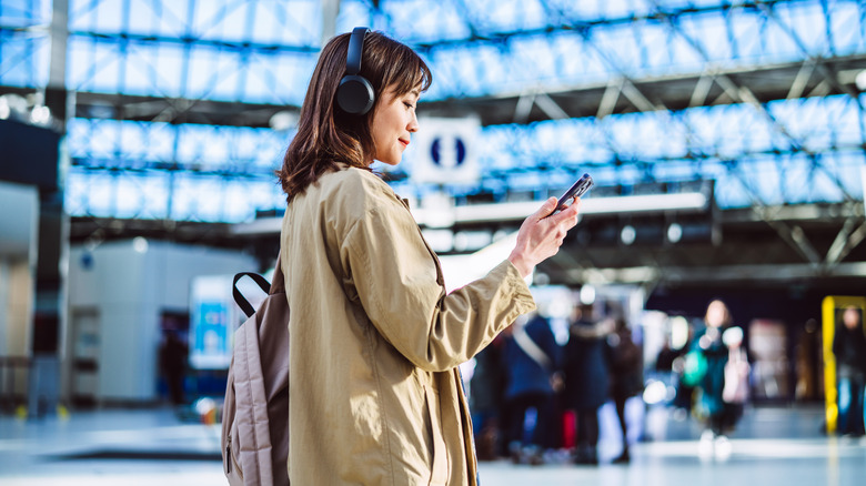 Woman in airport wearing headphones and looking at smartphone