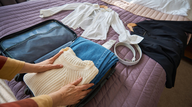Person packing a suitcase on top of a bed.