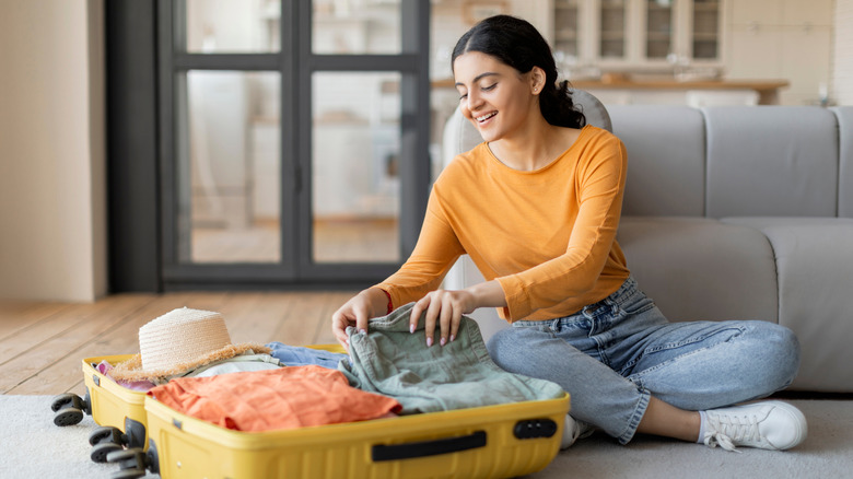 Smiling woman packing clothes into luggage