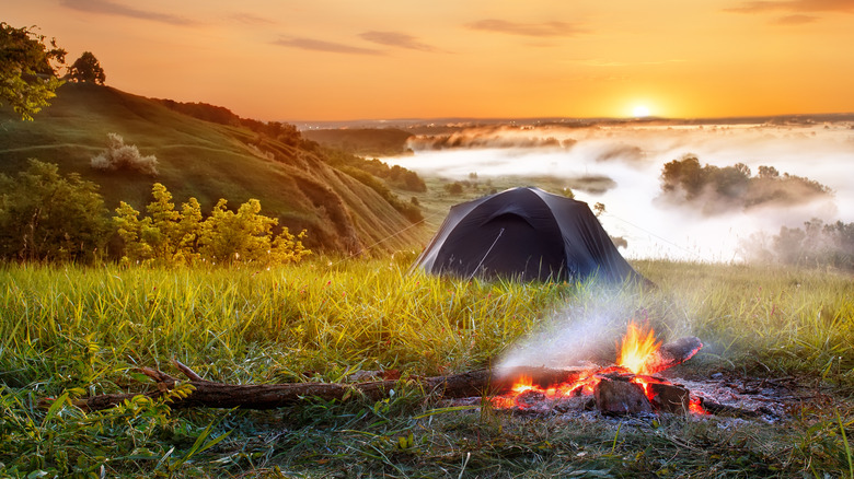 Tent and campfire on a scenic hill during sunset.
