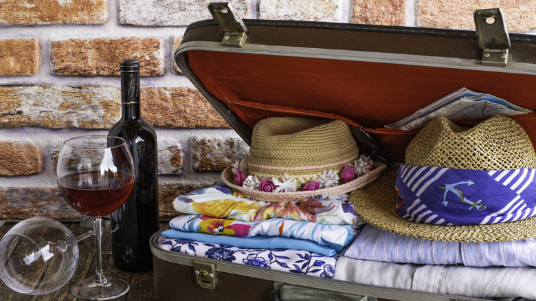 Wine bottle and glass next to an open, red-lined suitcase