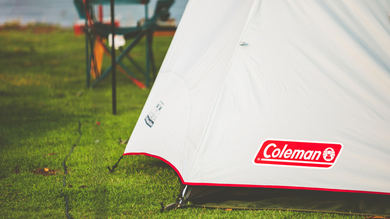 A Coleman tent stands on a grassy campsite