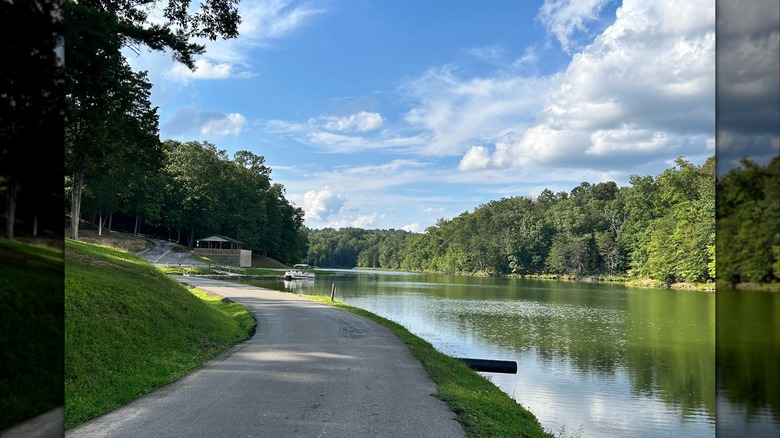 A paved path alongside Yatesville Lake at Yatesville Lake State Park, Kentucky, surrounded by greenery under a partly cloudy sky