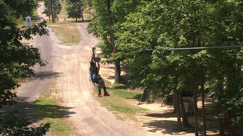 A zipliner hovering above a path in the woods at Kersey Valley Attractions in Archdale, North Carolina