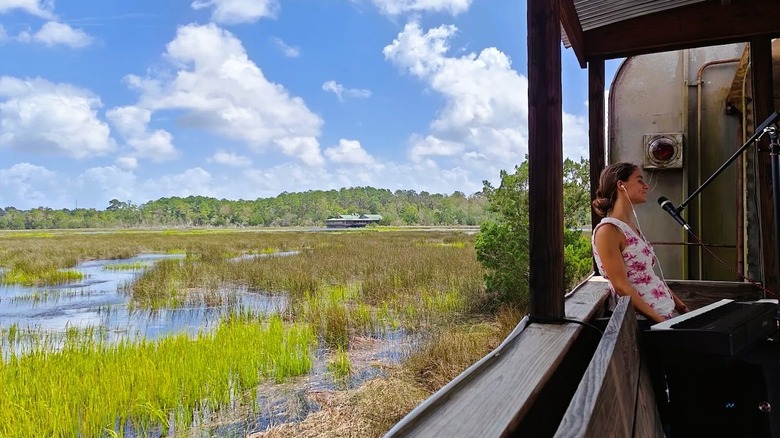 A performer riding in an open air train car on the Georgia Coastal Railway, with views of a grassy wetland.