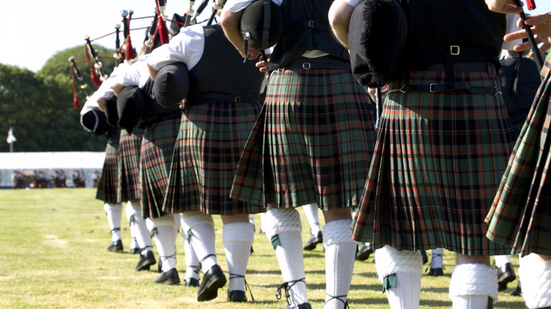 Bagpipers participate in traditional Scottish military tattoo by walking in a single file line, all dressed in kilts