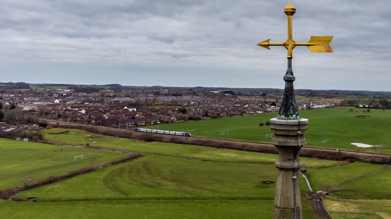 Arrow weathervane topper with green valley in background crossed by train tracks
