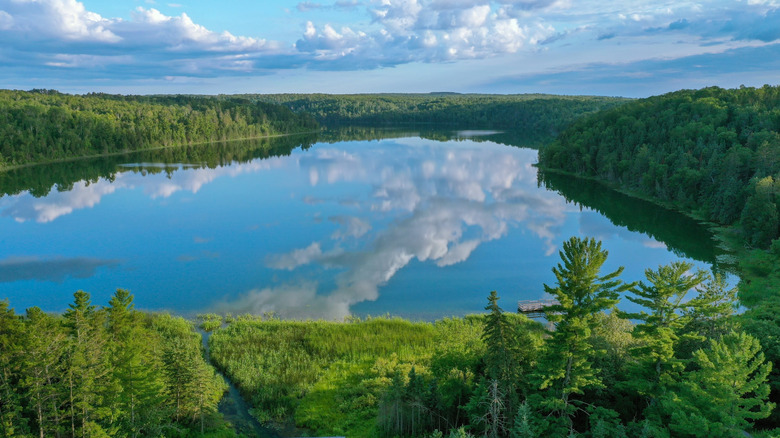 Trees surrounding a still La Salle Lake, with blue sky and cloud reflections