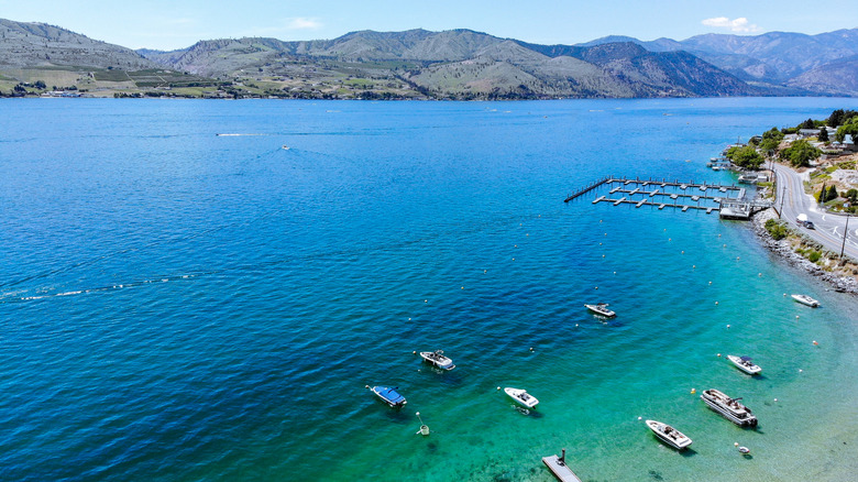 Aerial view of boats on the blue water of Lake Chelan around a marina with mountains and roads on either side