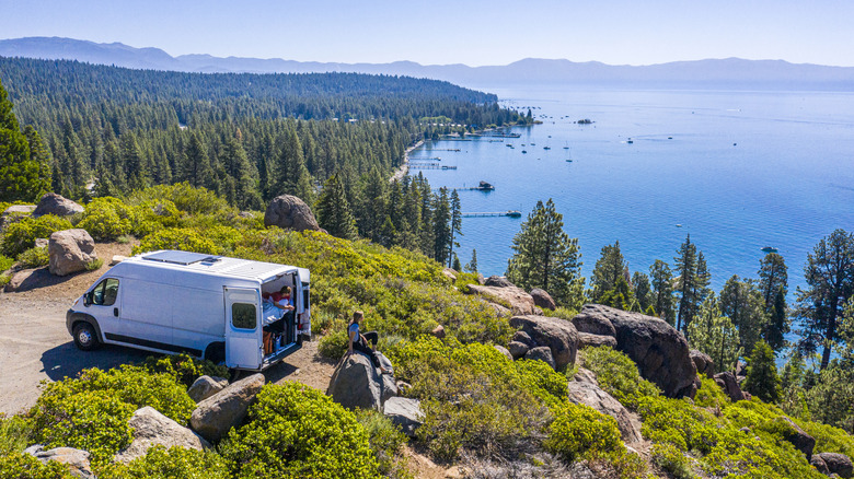 A van is parked on the edge of a forest overlooking Lake Tahoe on a sunny day