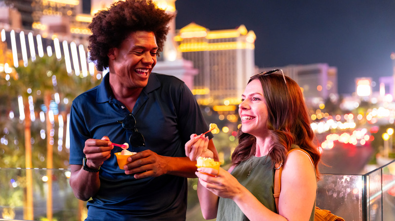 A smiling, happy couple enjoying ice cream together on the Las Vegas Strip, lit up but blurred in the background