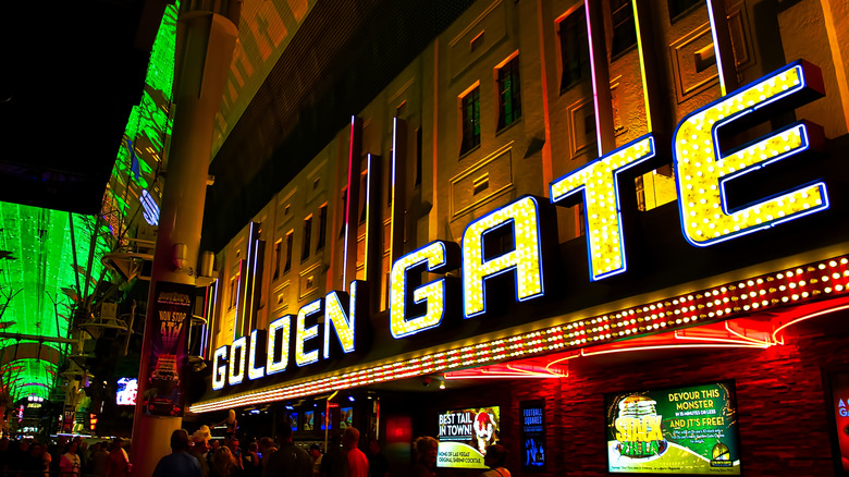 Golden Gate spelled out in bright yellow letters at the Golden Gate Hotel & Casino in downtown Las Vegas with the green of the Fremont Street canopy in the background.