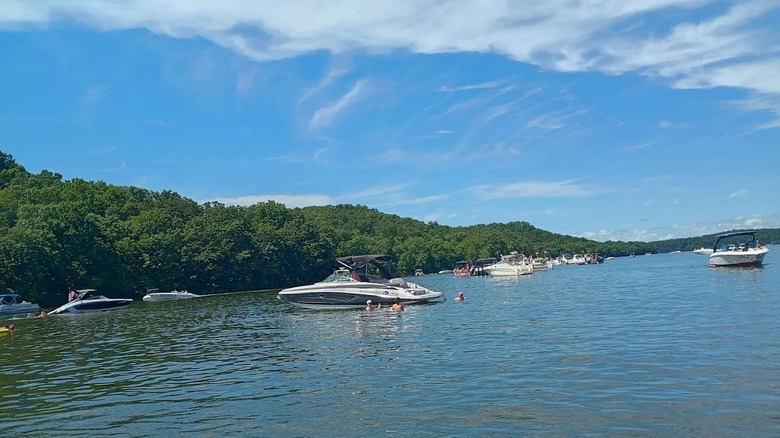 Multiple boats drifting on the calm waters at Lake of the Ozarks State Park, surrounded by lush rolling hills.