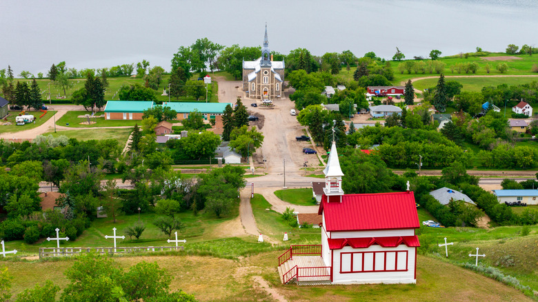 The Stations of the Cross in Lebret located on a hill overlooking the village with a 1929 wood-frame chapel, houses, a church, trees, and lake.