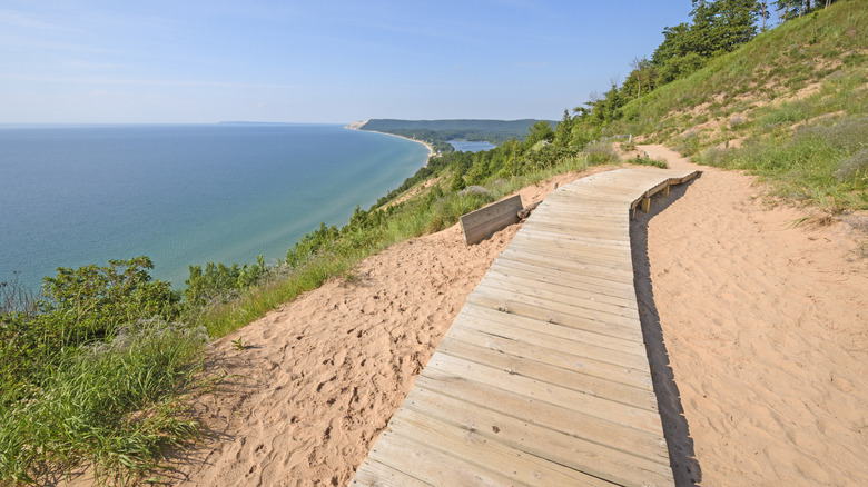 A wooden boardwalk winding along a sandy dune on the Empire Bluff Trail, overlooking the waters of Lake Michigan