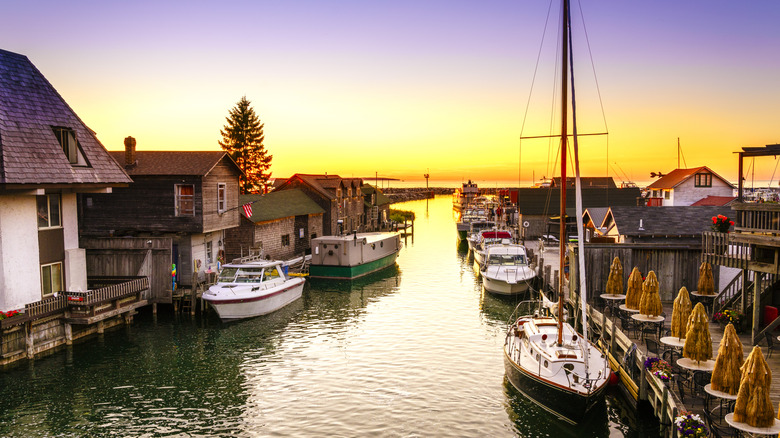 Boats and sailboats docked along wooden shanties and a waterfront patio at golden hour in Leland's historic Fishtown