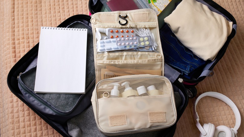 a suitcase lying open with clothes and a foldable toiletry pouch on top