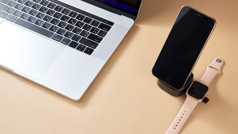 a laptop next to a phone and watch charging on a wireless charger