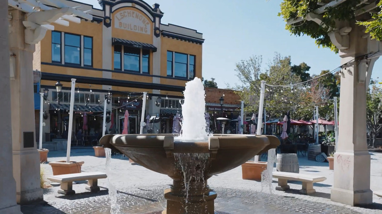 Stone fountain with benches and pillars around it and the L Schenone Building in the background
